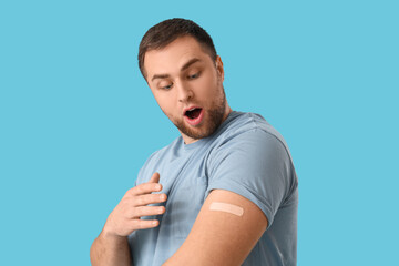 Young man with applied medical patch on blue background. Vaccination concept
