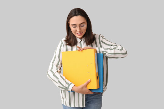 Young businesswoman with document folders on light background