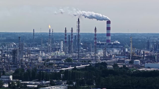 Aerial view of ORLEN Plock Production Plant with industrial towers, pipes, and a tall smokestack emitting smoke in Plock, Masovian Voivodeship, Poland.