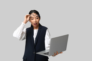Portrait of surprised Asian businesswoman with modern laptop on grey background