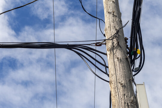 La Tuque, Quebec, 08 May 2026 : Numerous black electrical and communication cables are bundled and attached to a wooden utility pole against a cloudy blue sky.