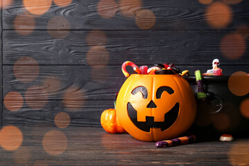 Naklejka premium Halloween celebration and trick or treat tradition, jack o lantern pumpkin bucket filled with assorted candy on dark wooden background with bokeh lights