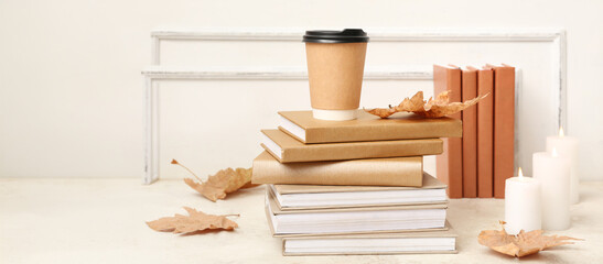Cozy autumn reading and relaxation, paper coffee cup on a stack of books with dry leaves and...