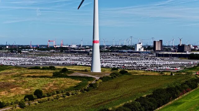 Aerial view of the Volkswagenwerk Emden automotive plant with rows of parked cars and wind turbines under a clear blue sky in Emden, Niedersachsen, Germany.