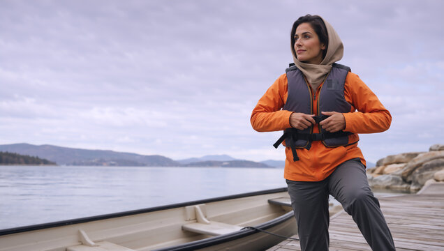 Woman fastening a life jacket on a wooden dock next to a boat. Outdoor water safety and adventure concept. Active lifestyle by the lake