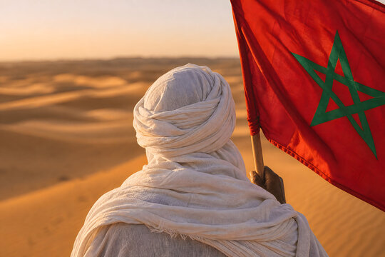Sahraoui man wearing traditional white tagelmust turban holding moroccan flag close up rear view blurry desert dunes