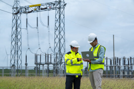 Power engineer inspecting electrical substation equipment with laptop and safety vest during outdoor maintenance planning
