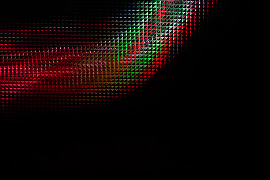 Extreme close-up macro shot of a digital display screen revealing a glowing RGB pixel grid in vibrant red and green colors fading into a dark black background.