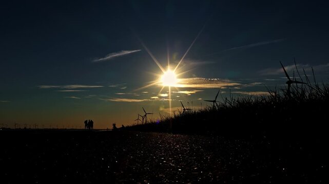 Aerial view of wind turbines silhouetted against a bright sunset sky in Emden, Niedersachsen, Germany.