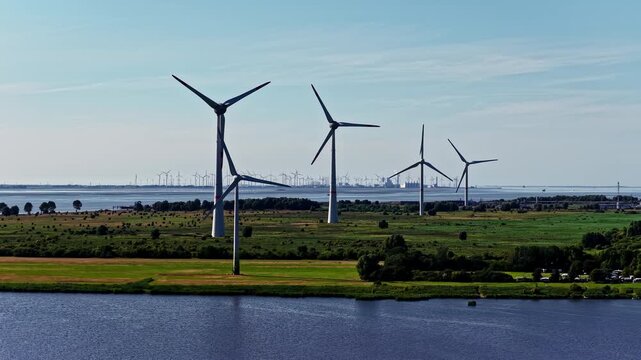 Aerial view of wind turbines in a green landscape with the Volkswagenwerk Emden factory in the background in Emden, Niedersachsen, Germany.