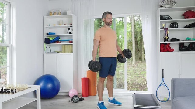 Dumbbells exercise for arms and shoulders. Man focused on dumbbells workout. Home strength training with dumbbells. Fitness lifestyle with home dumbbells. Man using weights for daily workout.