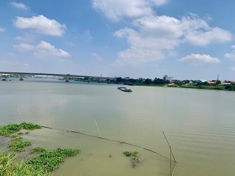 Wide river landscape with a long bridge and a sand dredging barge boat in Cambodia under a bright blue sky
