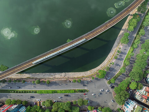 Aerial view of metro train crossing Dong Da Lake beside busy roads in Hanoi, Vietnam