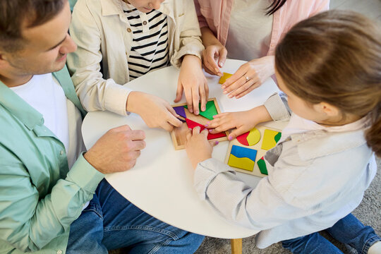 Family parents children playing puzzle game together. Parents help kids arrange shapes on a home table, boosting teamwork and creativity. Warm family bonding and teamwork concept here.
