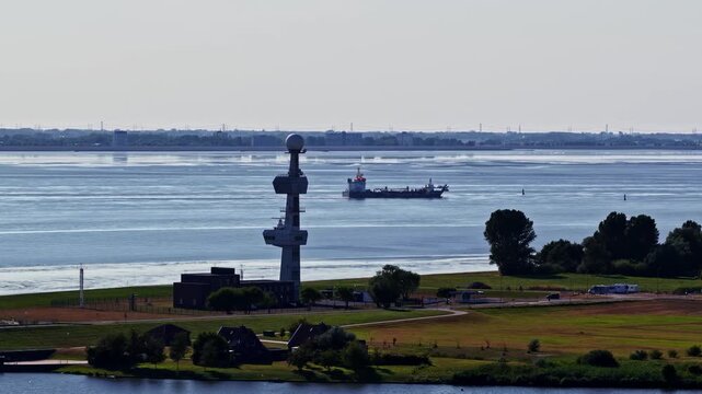 Aerial view of the radar tower overlooking the Ems estuary with a cargo ship in the distance in Emden, Niedersachsen, Germany.