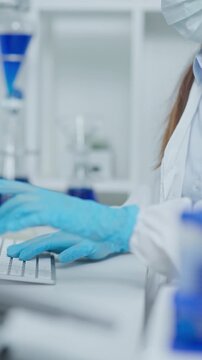 Close-up of a laboratory professional wearing blue gloves typing on a computer while reviewing test data in a clean clinical research environment.