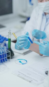 Close-up of a medical laboratory technician examining a sample and writing notes on a report in a clean clinical laboratory environment.