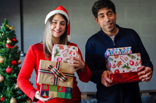 Smiling Hispanic couple holding stacks of Christmas presents looking at camera