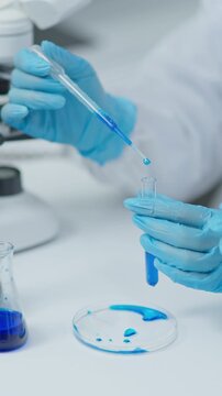 Laboratory technician transferring liquid sample into a test tube with a pipette in a clean clinical laboratory during scientific analysis.