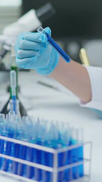 Laboratory professional holding and checking a test tube containing blue liquid sample during analysis in a clean clinical research environment.