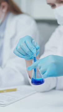 Laboratory professional holding and checking a test tube containing blue liquid sample during analysis in a clean clinical research environment.
