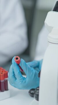 Close-up of a laboratory technician holding a blood sample test tube during medical testing and laboratory analysis in a clean clinical environment.