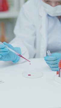 Close-up of a laboratory technician using a pipette to place a blood sample into a petri dish during medical research and laboratory testing.