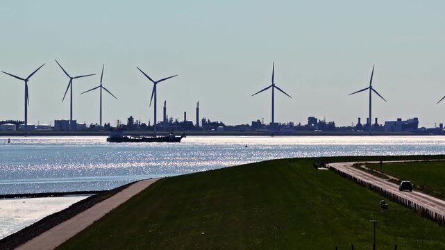 Aerial view of the Volkswagenwerk Emden industrial plant with wind turbines, a cargo ship on the river, and a coastal road in Emden, Niedersachsen, Germany.