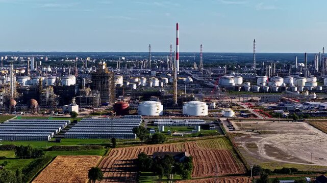 Aerial view of the Orlen Plock Production Plant with large storage tanks, tall chimneys, and industrial infrastructure near fields in Plock, Mazowieckie Voivodeship, Poland.