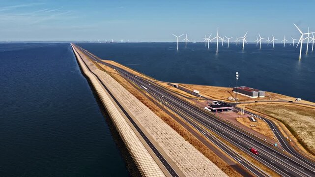 Aerial view of Windpark Fryslan offshore wind turbines and the Afsluitdijk causeway with highway traffic in Breezanddijk, Friesland, Netherlands.
