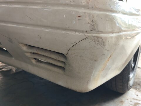 A detailed close up view of a damaged white car bumper showing cracks, scratches, and rust stains, highlighting vehicle body damage, collision repair work, and automotive maintenance.