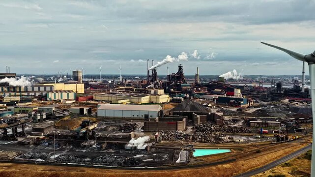 Aerial view of the extensive Tata Steel industrial complex with smoking chimneys and wind turbines in Velsen-Noord, Noord-Holland, Netherlands.