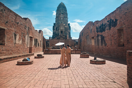Asian traveler family, mother and child dressed in traditional Thai outfit with umbrella in sunny, summer holiday travel in Ayutthaya, Southeast Asia, ancient ruins heritage,  tourist destination.