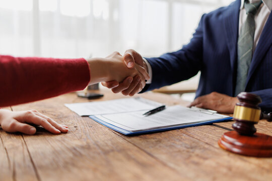 Professionals shaking hands, signing an agreement or contract, finalizing a legal settlement, partnership, or business deal, signifying justice and mutual understanding