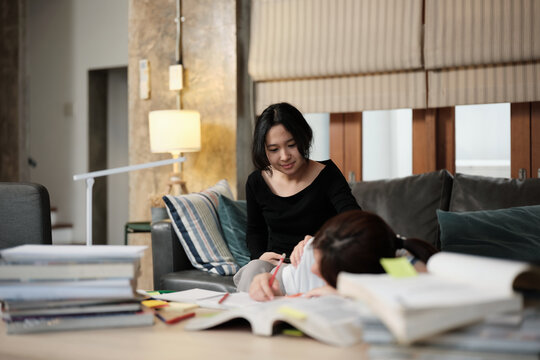 Two College Asian friends, teenage girl tired and burned out from overwhelmed homeschooling, study pile of books, stressed learning at home, her friend wakes up while napping, education exam support.