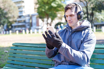 Fototapeta premium Man using smartphone and headphones on park bench