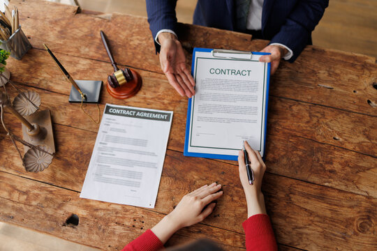 Client signing a legal contract agreement with a lawyer, reviewing paperwork and terms, symbolizing a business transaction, justice, and important administrative work