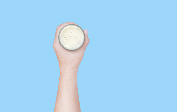 A hand holding a glass of milk against a blue background, top view.