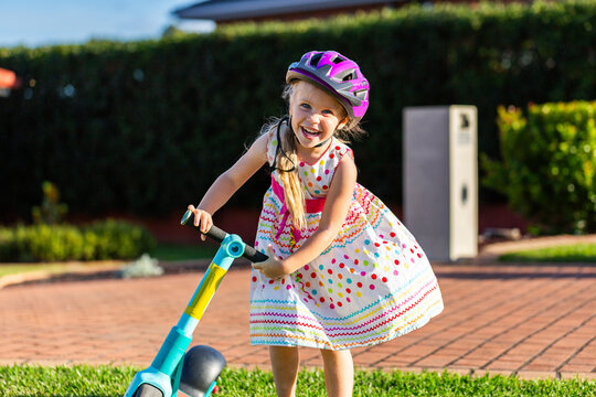 Happy Australian preschooler girl riding scooter in front yard of suburban home