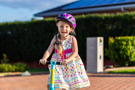 Happy Australian preschooler girl riding scooter in front yard of suburban home