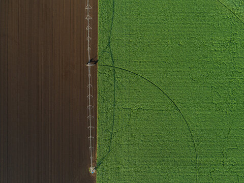Irrigation sprinkler alongside lush green paddock with tilled land of fertile soil