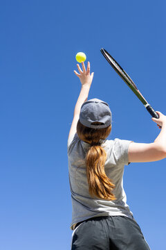 Young tennis player tosses the ball high for a perfect serve under a clear blue sky