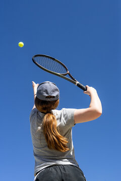 Young tennis player tosses the ball high for a perfect serve under a clear blue sky