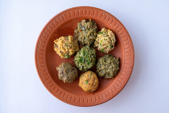 Traditional Bengali mashed side dishes with potato, eggplant, fermented dry fish, small fish, lentil, and long beans arranged in a terracotta dish. Top view.