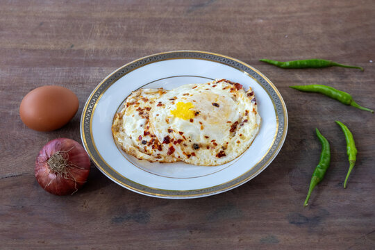 Spicy Fried Egg Poach with Chili Flakes, Traditional Bangladeshi Breakfast Dish, Whole Raw Egg, Onion, Green Chilies, Ceramic Plate on Wooden Background.