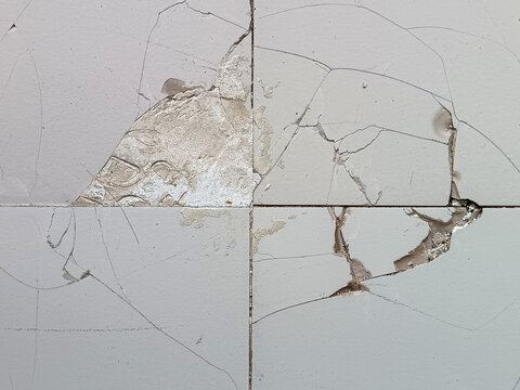 Close up view of heavily cracked and broken off ceramic tiles surface with exposed cement underlying base for construction damage background.