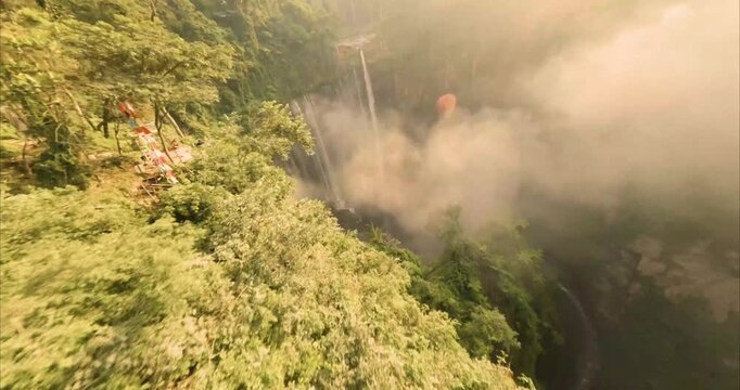 Aerial view of Tumpak Sewu Waterfall surrounded by lush tropical forest and mist in Kecamatan Pronojiwo, Jawa Timur, Indonesia.