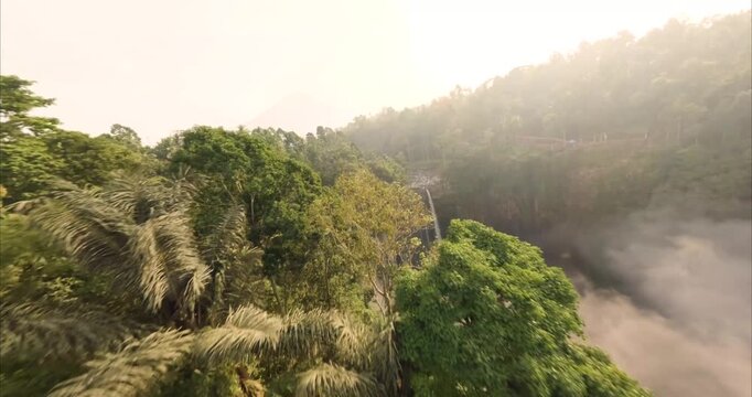 Aerial view of Tumpak Sewu Waterfall surrounded by lush tropical jungle and mist in Kecamatan Pronojiwo, Jawa Timur, Indonesia.