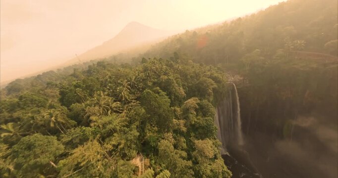 Aerial view of Tumpak Sewu Waterfall surrounded by lush tropical rainforest and steep cliffs in Kecamatan Pronojiwo, Jawa Timur, Indonesia.