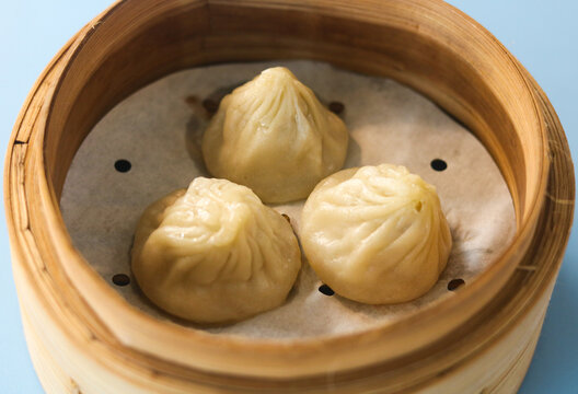 Three steamed xiao long bao soup dumplings served in a traditional bamboo steamer basket lined with parchment paper.